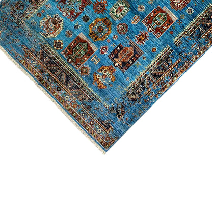 Close-up of a blue carpet corner with a border, fringes, and small patterned sections