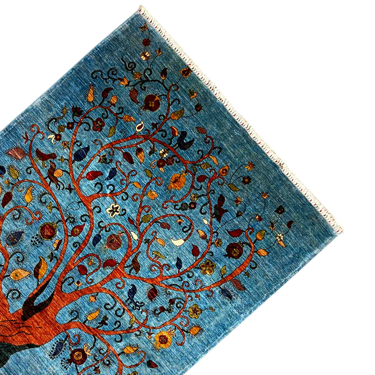 Corner of a blue rug with a tree motif, colorful flowers, and fringe