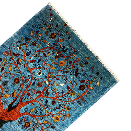 Corner of a blue rug with a tree motif, colorful flowers, and fringe