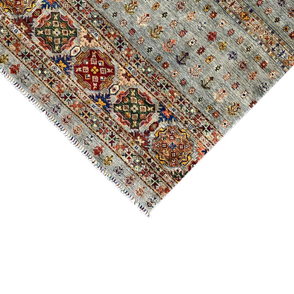 Corner of a hand-knotted Khorjin rug with ornaments and fringe on a light gray background