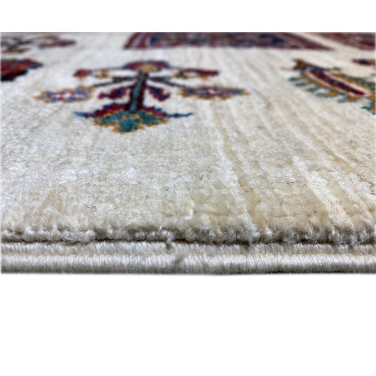 Khorjin rug edge detail with fringe and light pile on a cream-colored background.