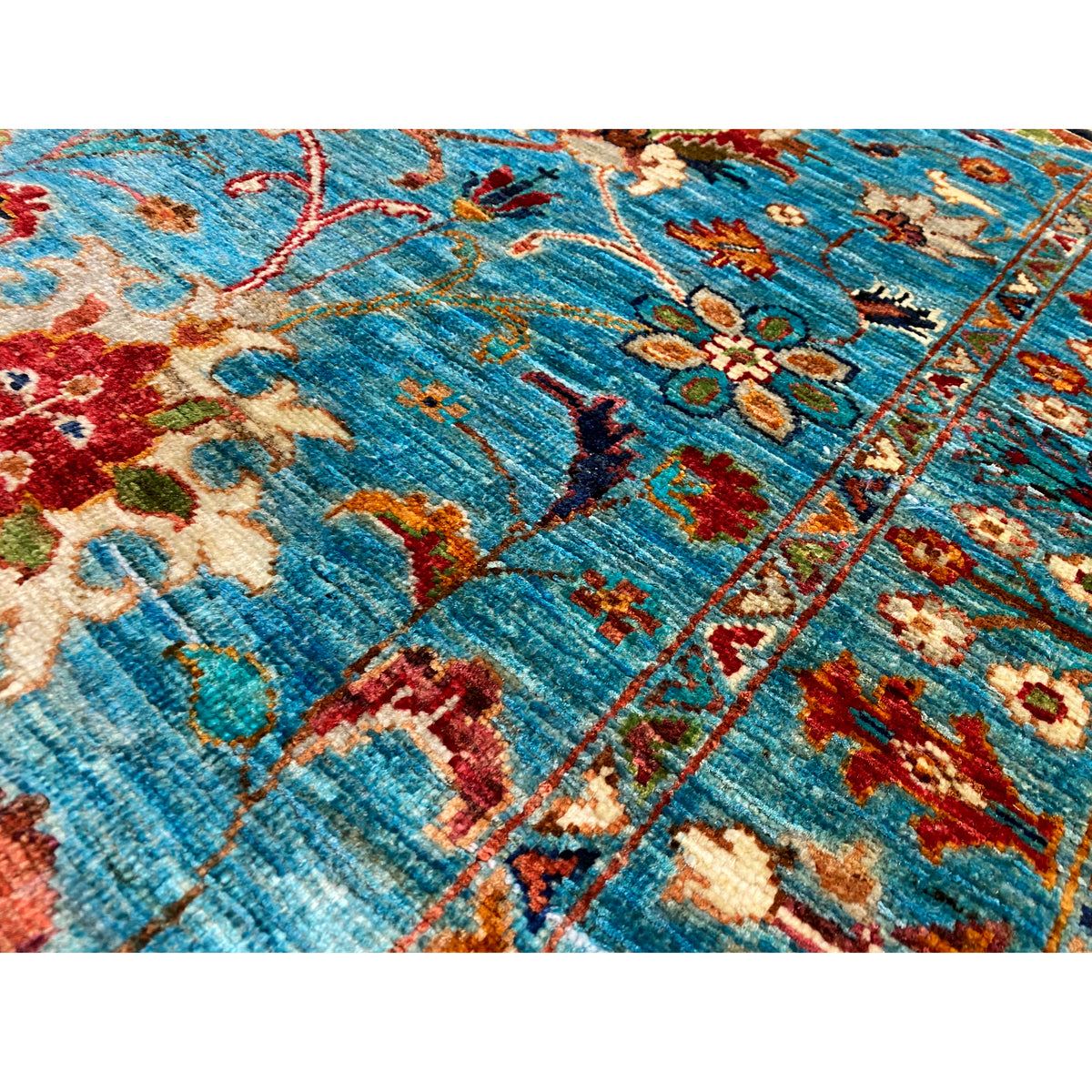 Close-up: blue woven carpet pattern with tendrils, multicolored embroidered details, pile