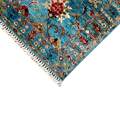 Close-up of the corner: blue carpet pattern with colorful flowers, white fringe
