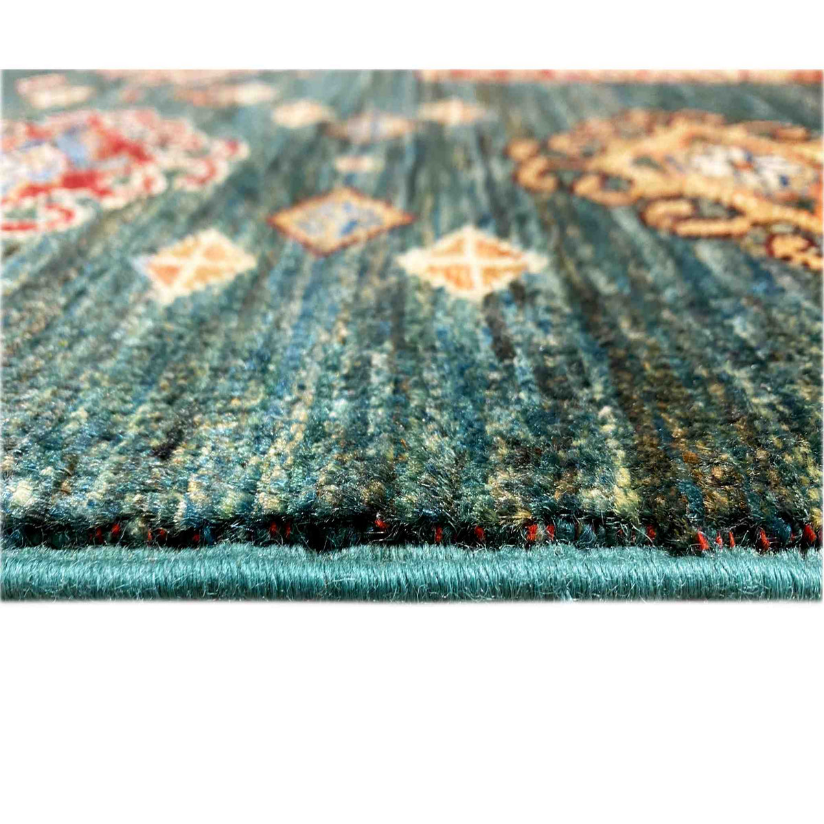 Close-up of carpet edge: blue-green pile with multicolored pattern and fringed finish