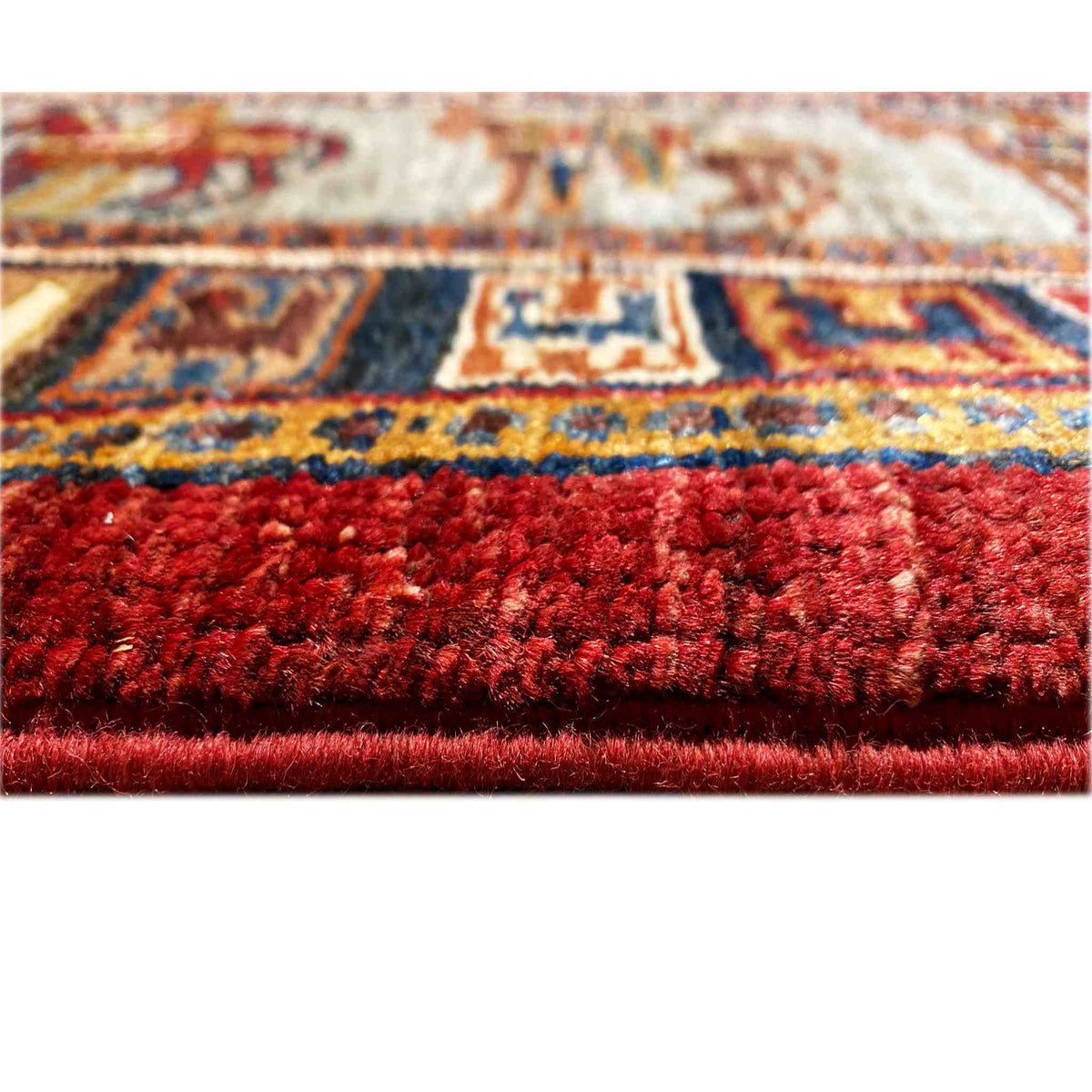 Close-up of the Khorjin carpet: dense red pile with colorful patterned borders in the background