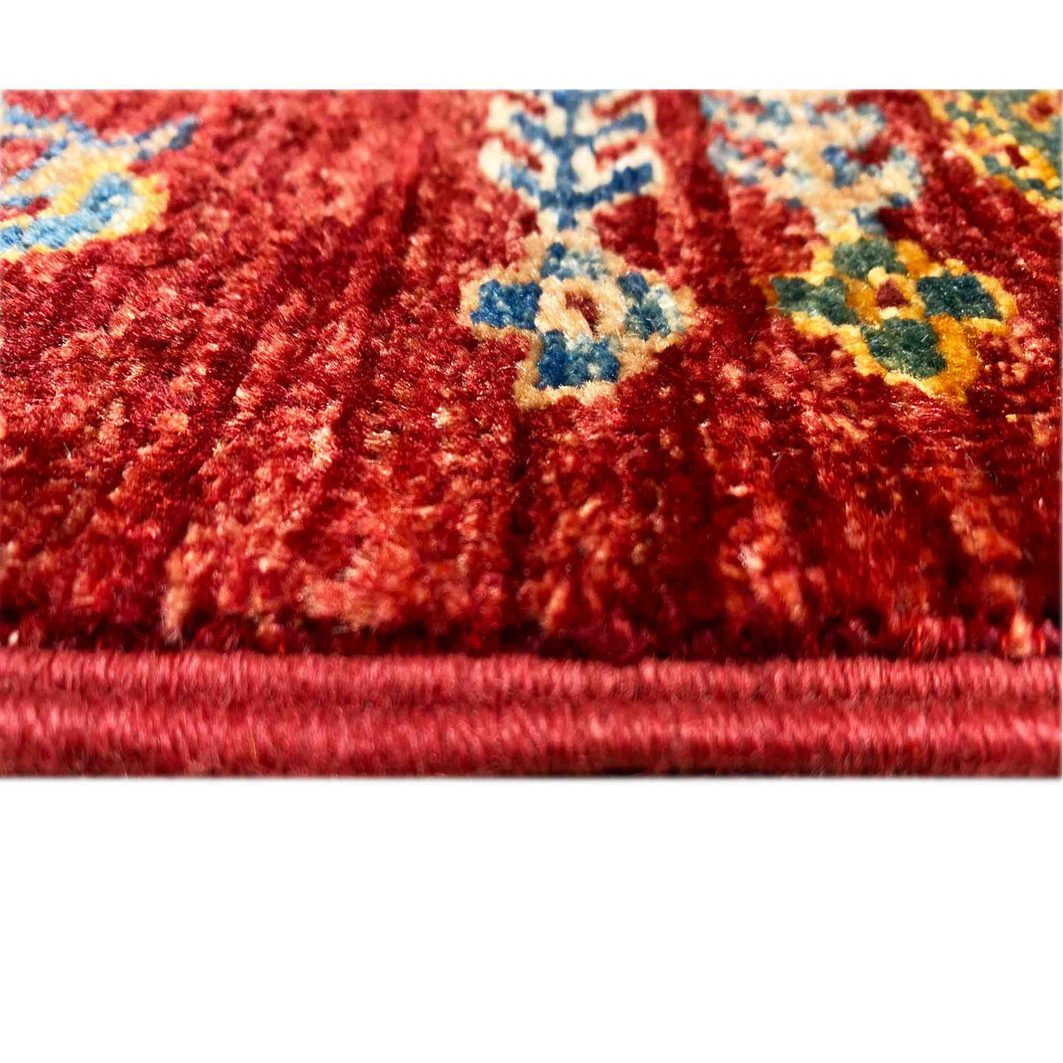 Close-up: red carpet pile with colorful patterns, visible fringes