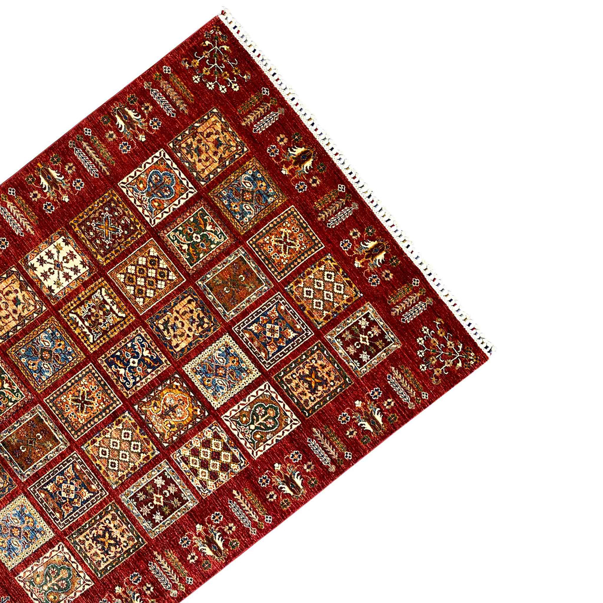 Corner of a red rug with colorful patchwork squares and a white fringed edge