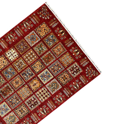 Corner of a red rug with colorful patchwork squares and a white fringed edge