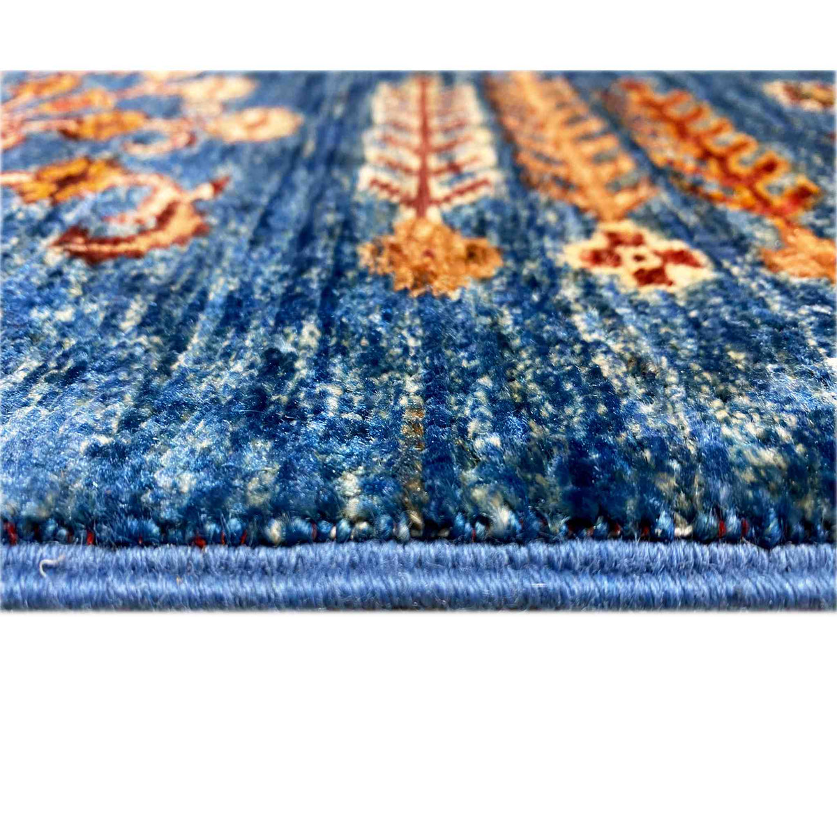 Close-up of a Khorjin rug: blue pile, colorful ornaments, and a visible fringed edge