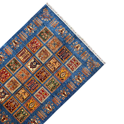 Khorjin rug at an angle: blue field with ornamental squares, border ornaments, and fringes