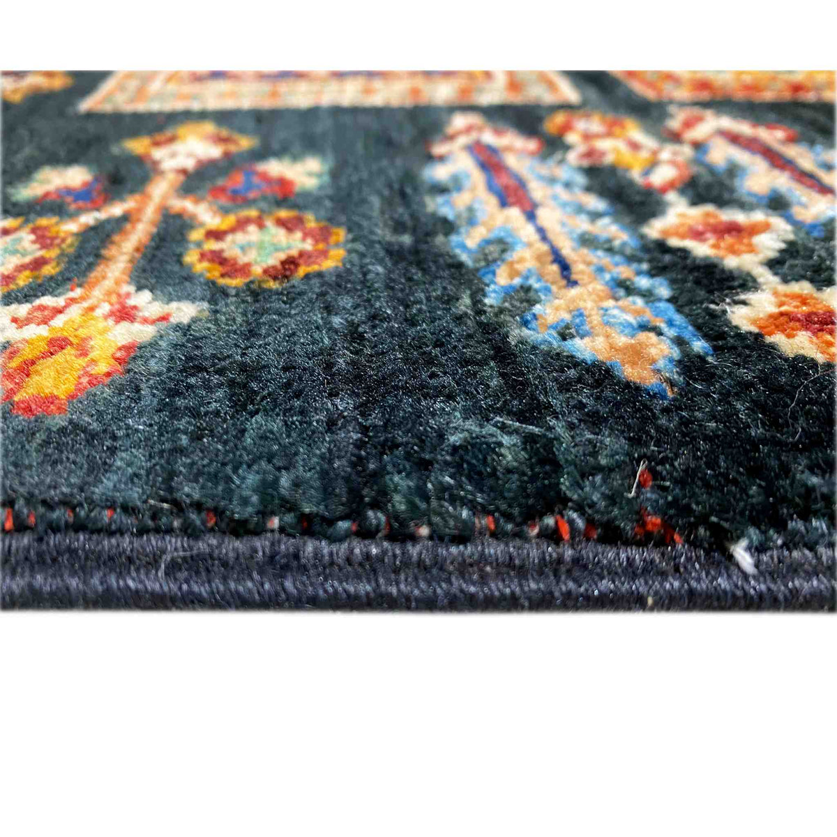 Carpet detail: dark pile with colorful accents and a jagged, fringed edge