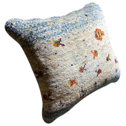Decorative cushion with a blue-and-white textured cover and colorful motifs, shown at an angle