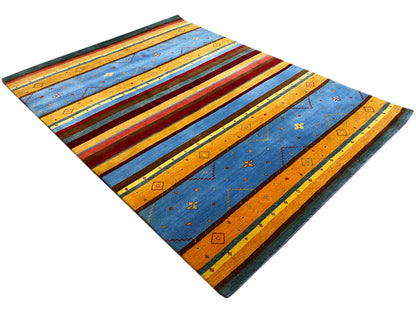 Loom Luri Teppich flach ausgebreitet: diagonale Ansicht mit blau-orangen Streifen und Mustern.
