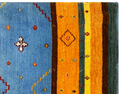 Loom Luri Teppich Detail: blaues Feld mit kleinen floralen Motiven, daneben orangefarbene Streifen.