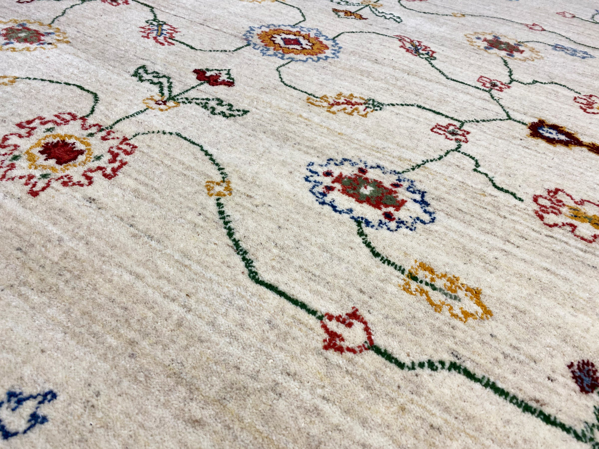 Teppichdetail in Creme mit bunten Ornamenten und feinen Linien, nah aufgenommen.