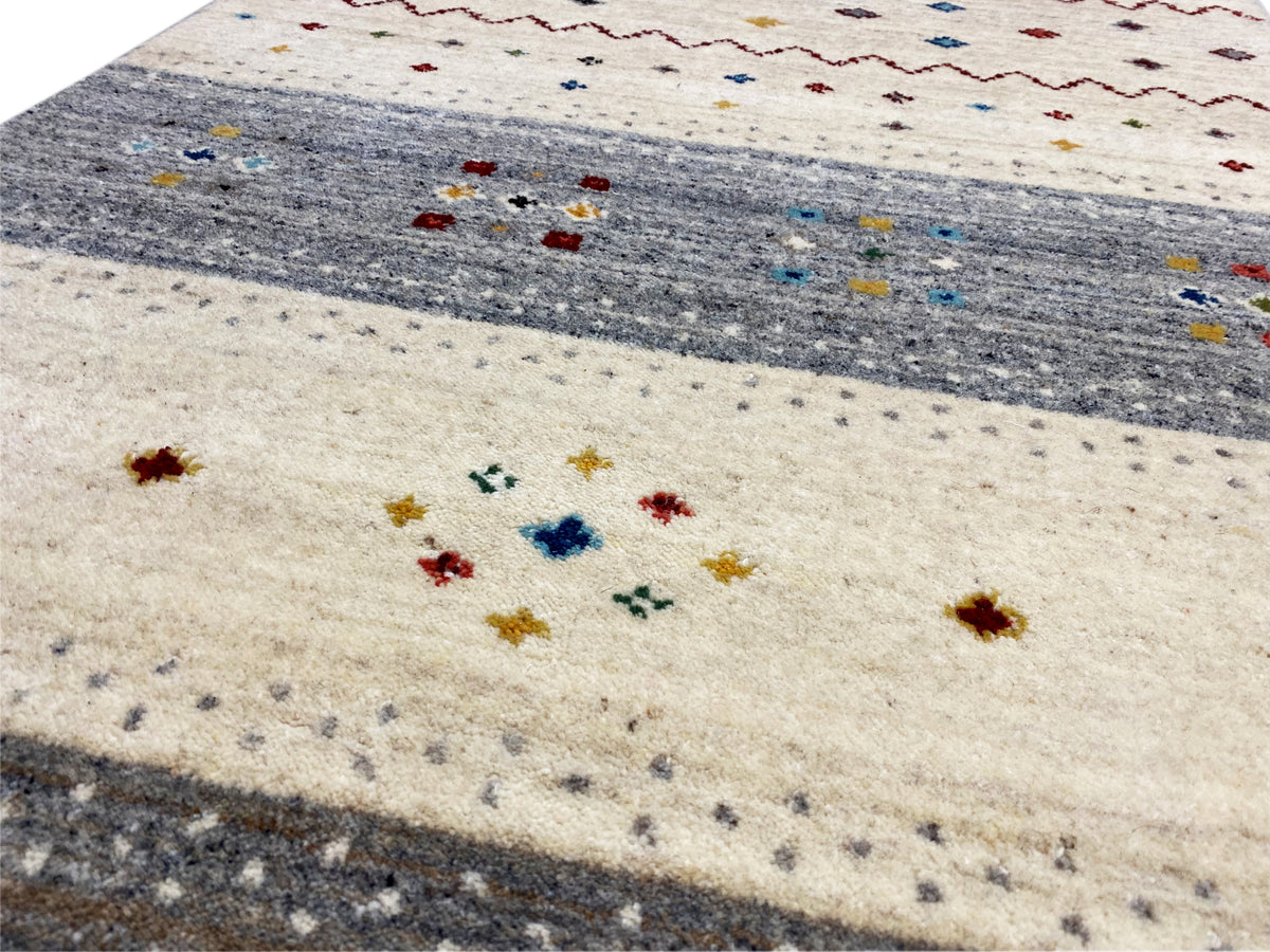 Nahaufnahme: beiger Teppich mit grauen Zonen und bunten Pünktchen und Ornamenten
