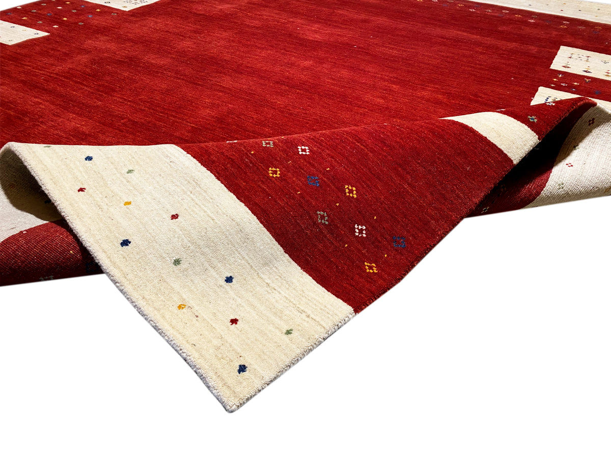 Roter Teppich mit beigem Rand und kleinen bunten Punkten, seitlich aufgeschlagenes Eck