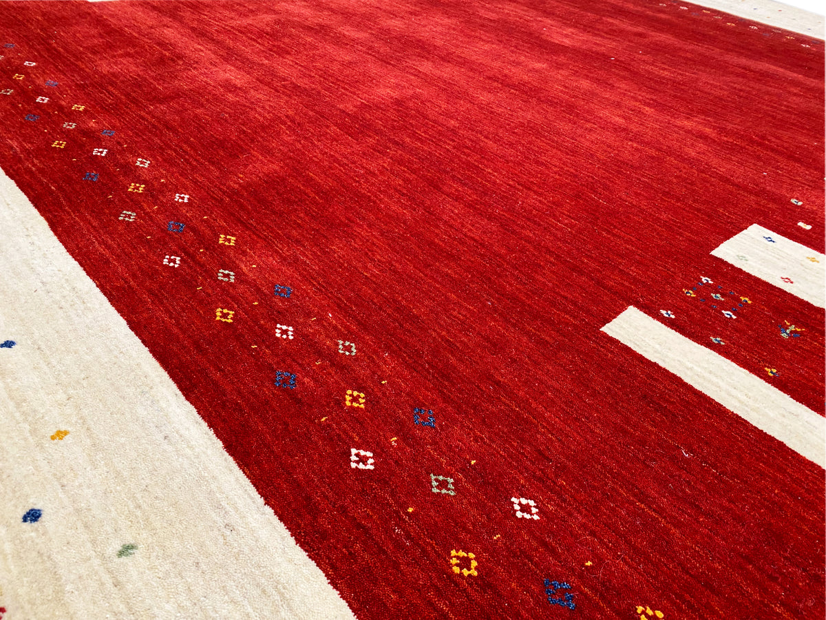 Nahaufnahme Teppich: rotes Feld mit farbigen Punkt- und Kreuzmustern sowie beigen Zierstreifen