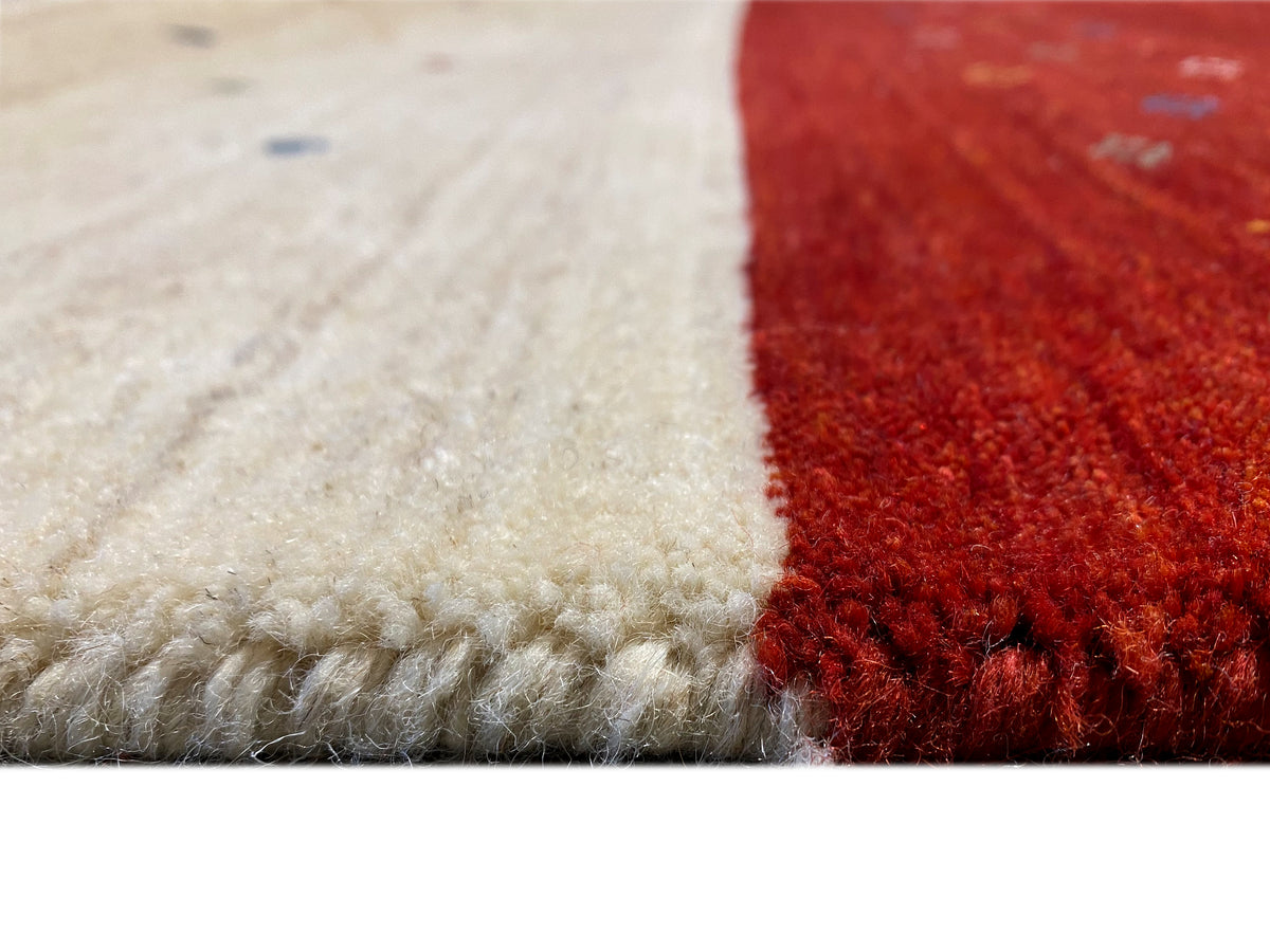 Teppichdetail an der Kante: beige Florfläche mit rotem Abschnitt und seitlicher eingefasster Naht