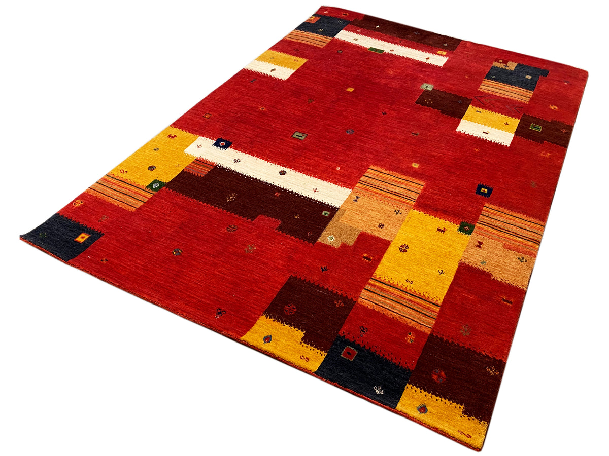 Loom Luri Teppich schräg gezeigt: rotes Patchwork mit gelben Streifen und dunkelblauen Feldern
