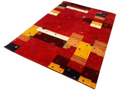 Loom Luri Teppich schräg gezeigt: rotes Patchwork mit gelben Streifen und dunkelblauen Feldern