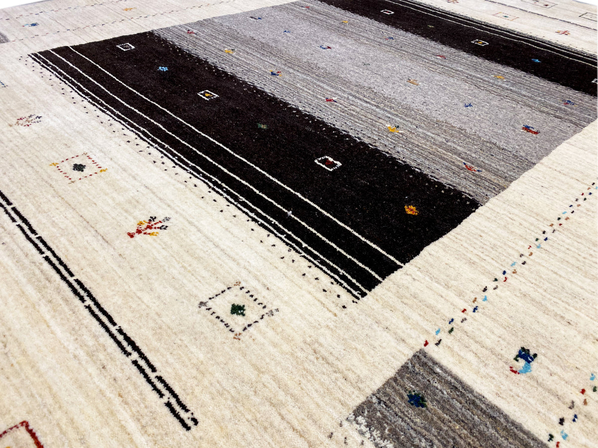 Detailansicht Loom Luri-Teppich: beiger Stoff mit schwarzen Linien, Punkten und farbigen Mini-Motiven
