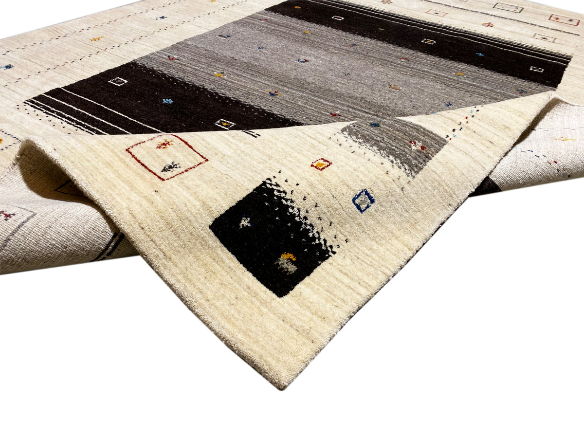Loom Luri-Teppich 240x176 cm Nahansicht: aufgerollte Ecke mit beige Flor und dunklem Innenmuster