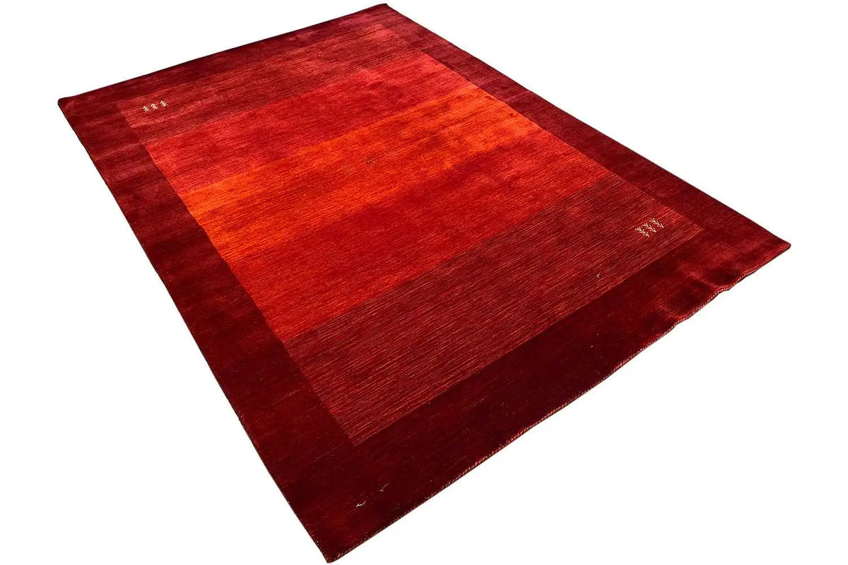 Red Gabbeh rug, laid out diagonally, with dark areas and small thread details.