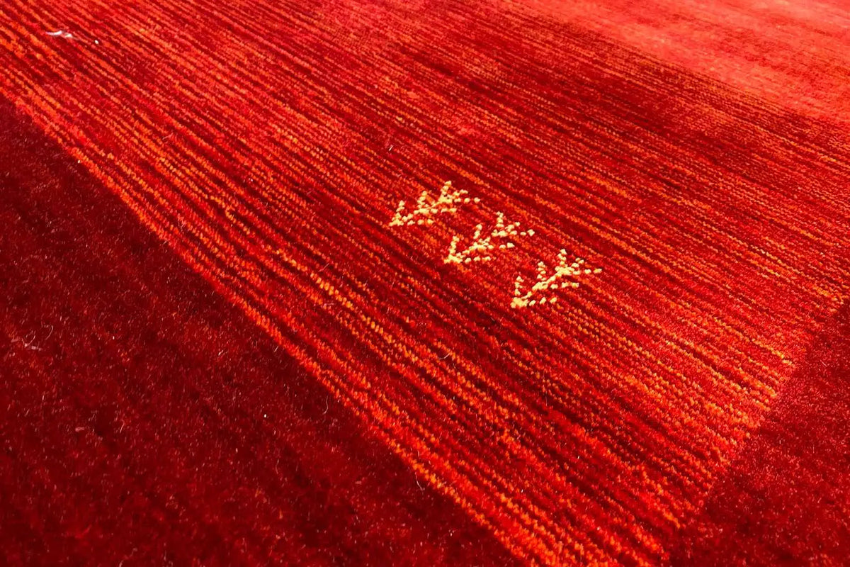Red Gabbeh rug with a gold-colored motif on a ribbed surface and fine texture.