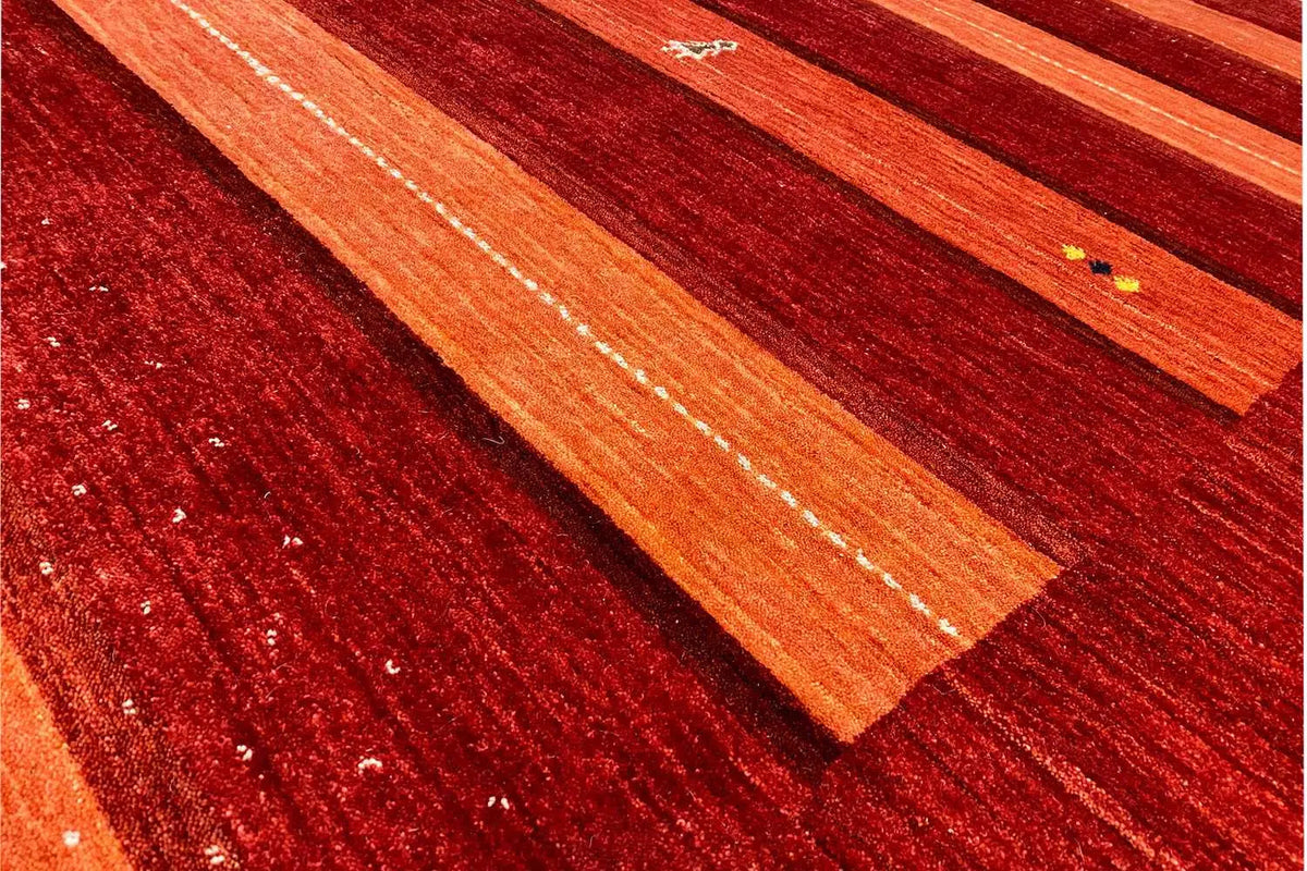 Detail view of the Gabbeh rug: orange stripes on a red background with shiny threads