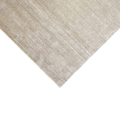 Corner of a beige low-pile rug, edges neatly bound, mottled texture