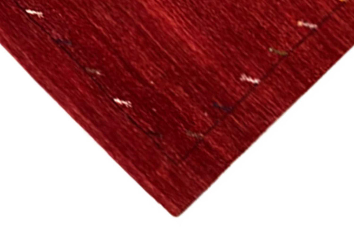 Corner of a red Gabbeh rug with a fine line pattern, clean edge