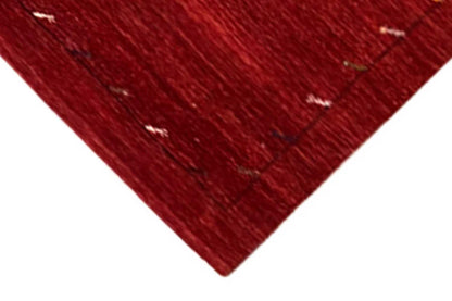 Corner of a red Gabbeh rug with a fine line pattern, clean edge