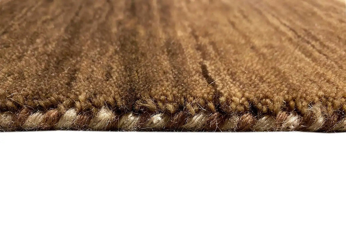 Gabbeh rug detail: brown pile texture and bound edge with tassel threads