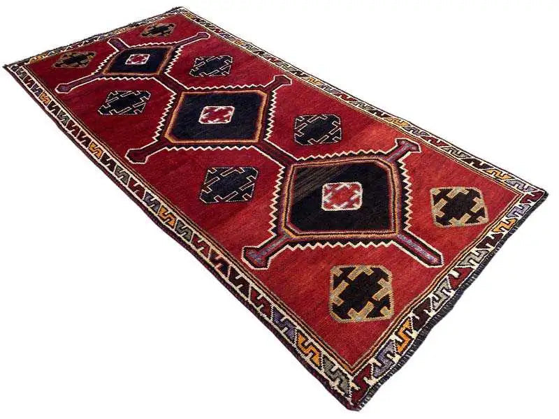Lori rug laid at an angle, with red areas, black squares, and colorful decorative bands along the edges.