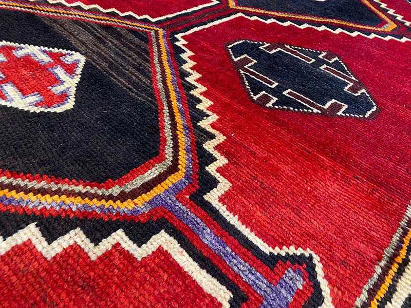 Lori rug detail: dark blue and red patterned areas with decorative lines in beige, yellow, and blue.