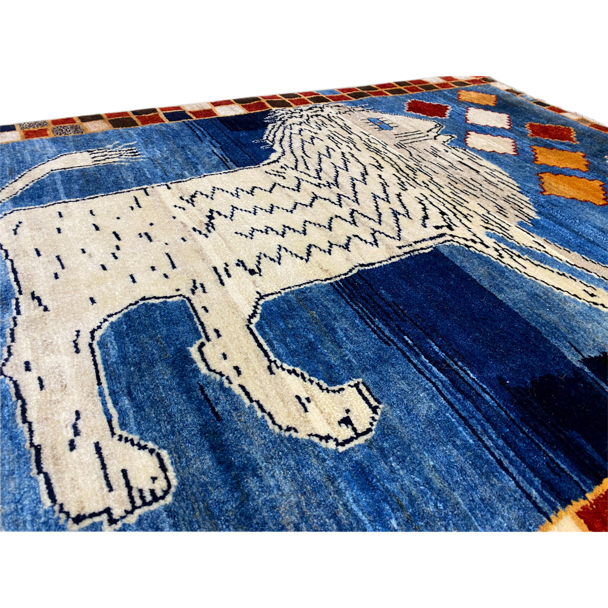Close-up: blue Gabbeh rug with a white lion motif and wave-like pattern lines.