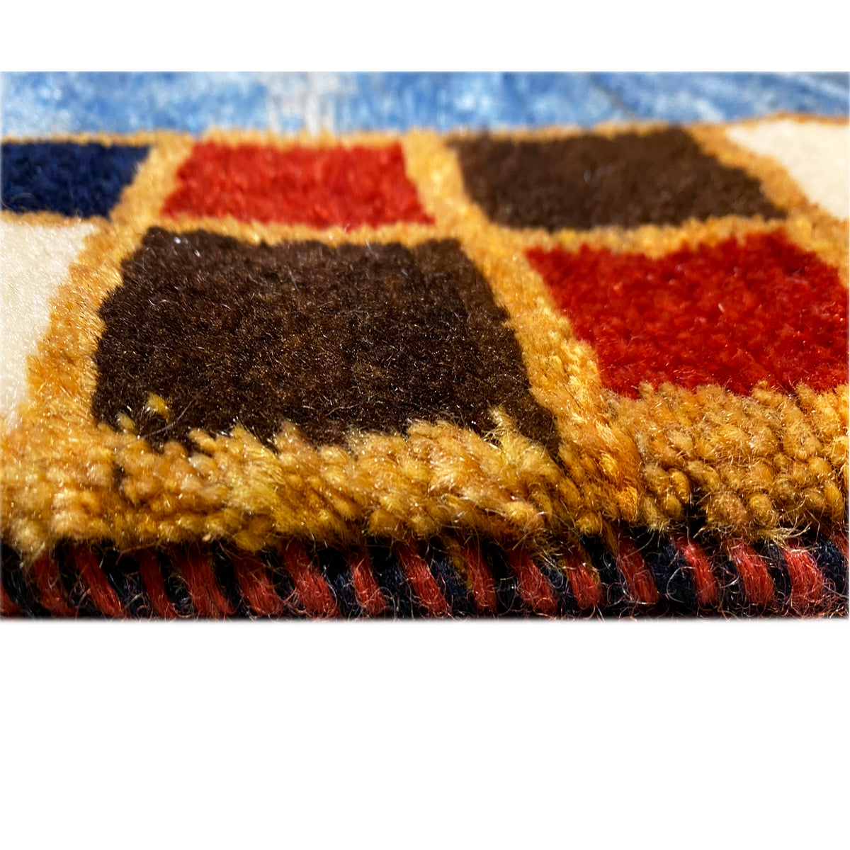 Close-up of carpet pile: multicolored fibers in blue, red, beige, and dark brown.
