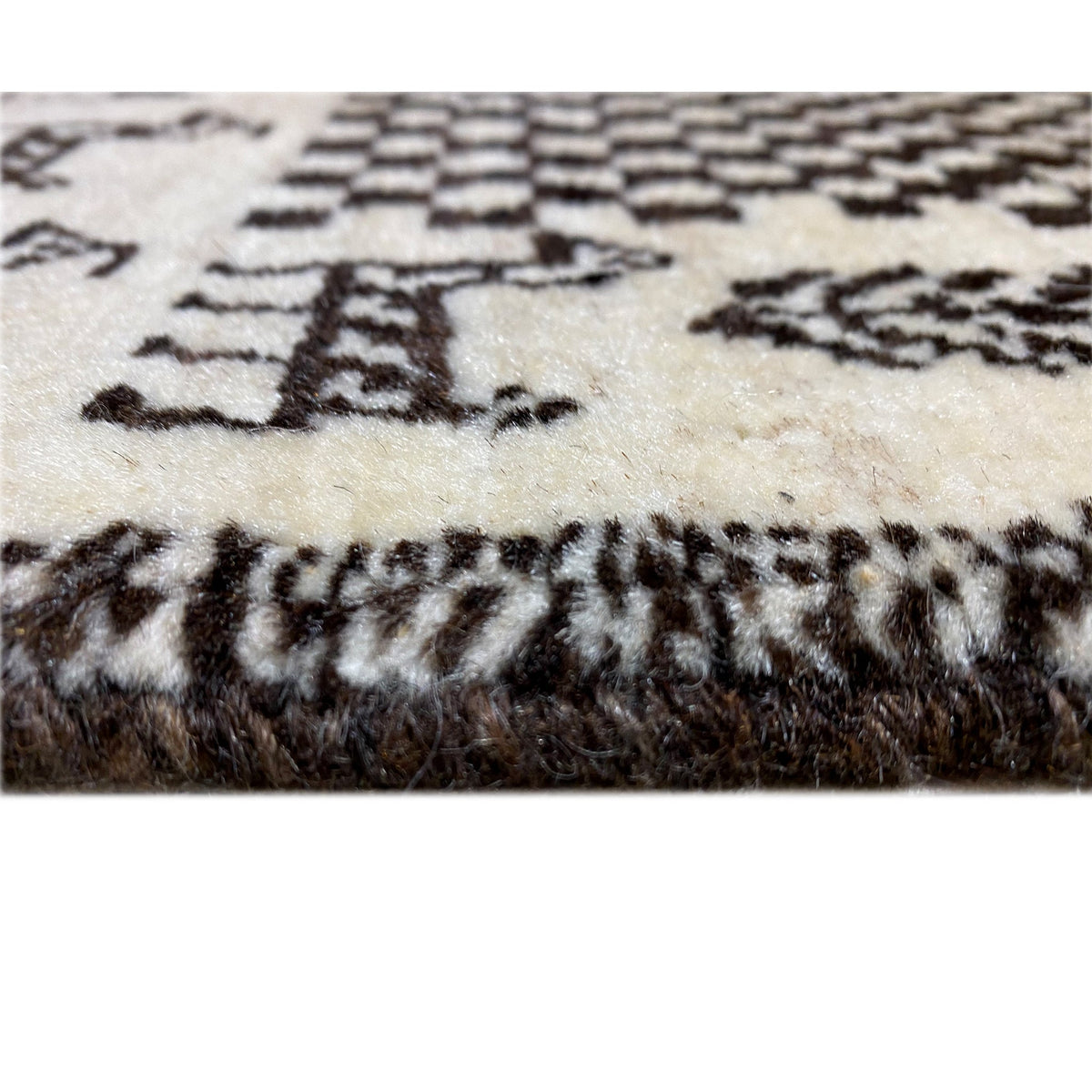 Detail of the carpet edge: Gabbeh rug with a black decorative pattern on a light background
