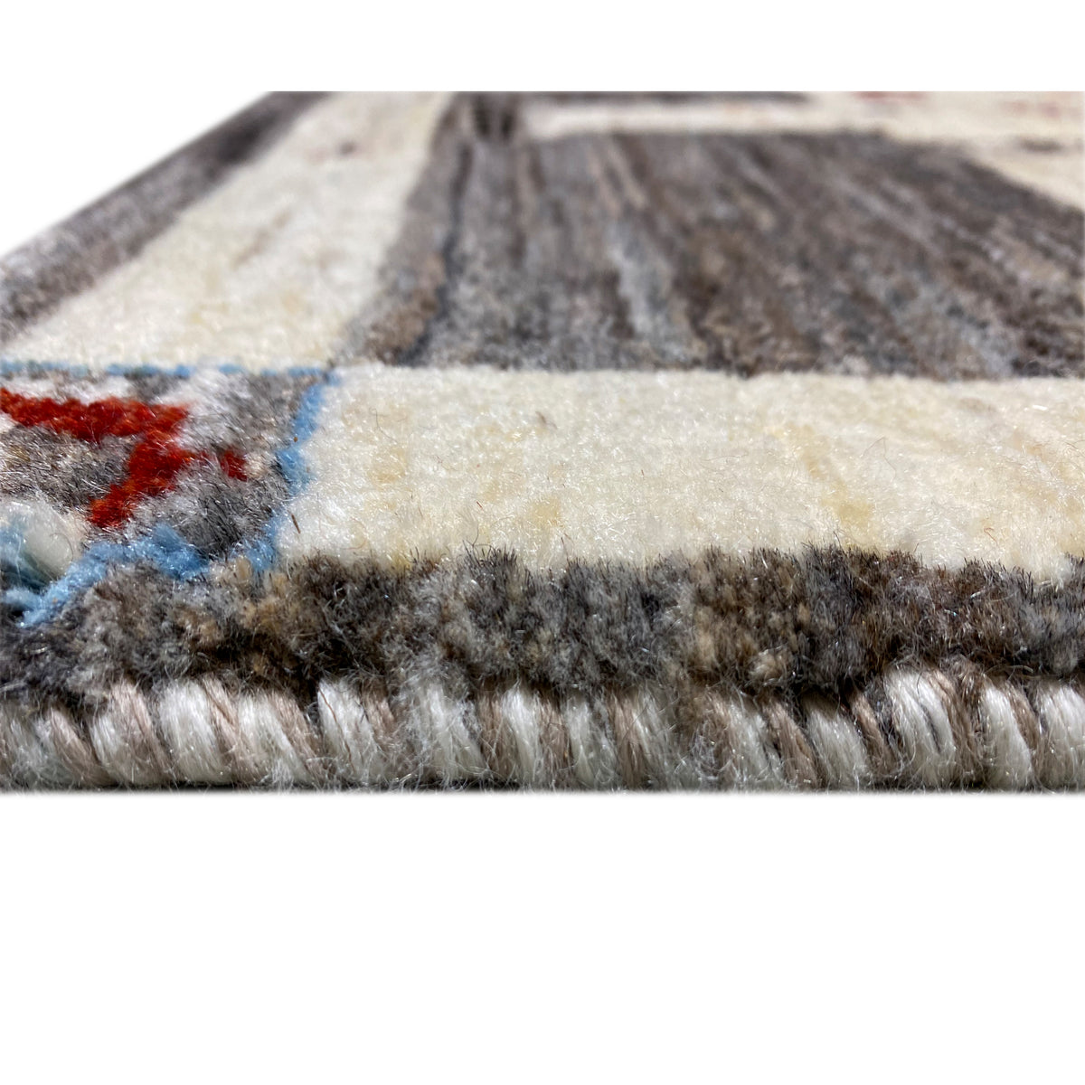 Carpet edge in detail: cream-colored base, dark gray pile, red and blue accents