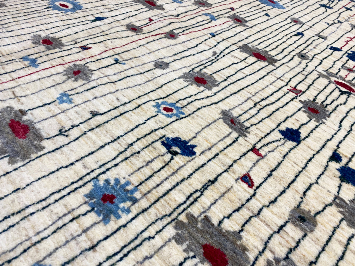 Nahaufnahme: cremefarbener Teppich mit blauen Linien, roten Akzenten und Musterblöcken