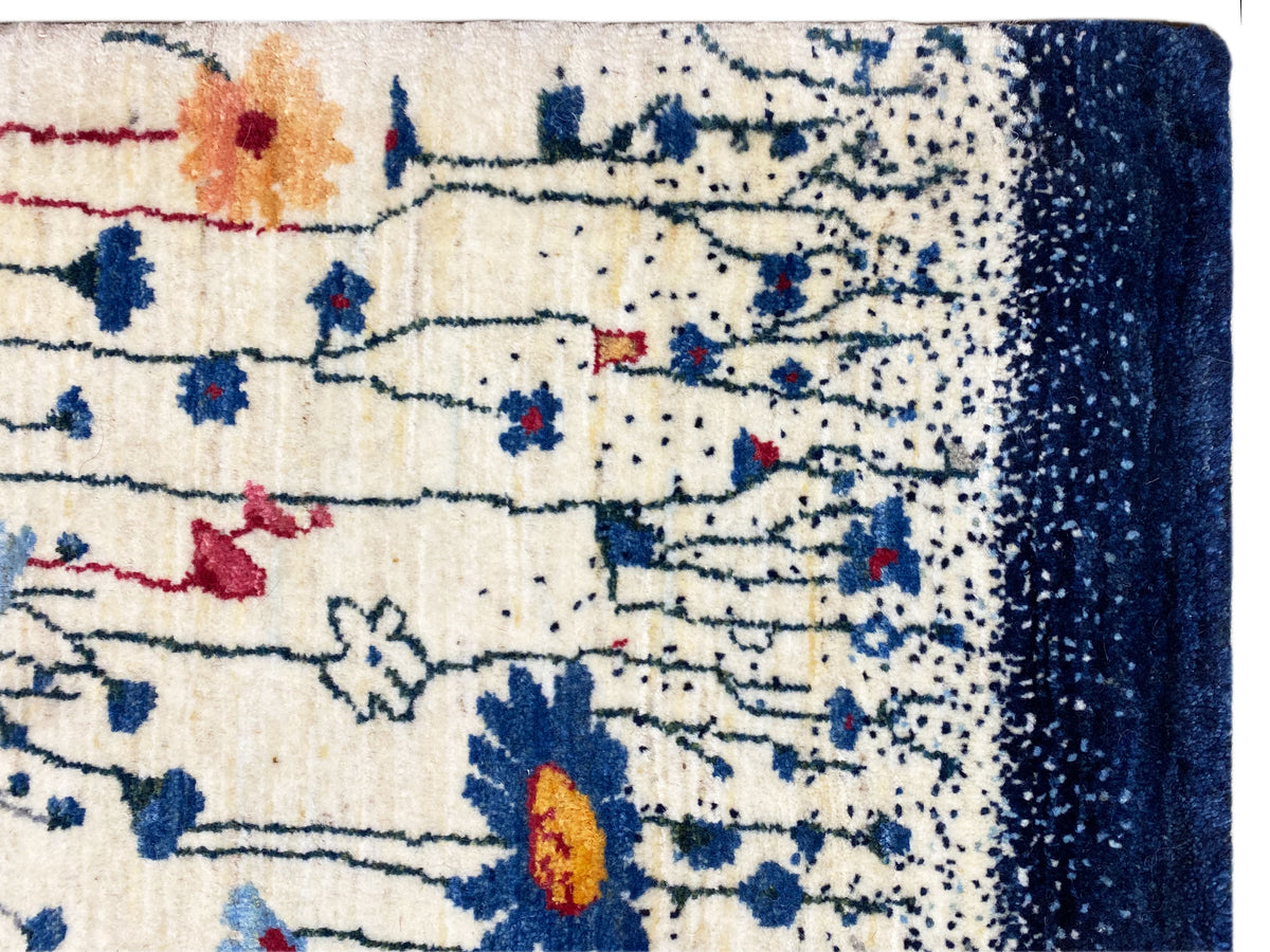 Detail am Rand: cremefarbener Teppich mit dunklem blauem Abschluss und bunten Motiven
