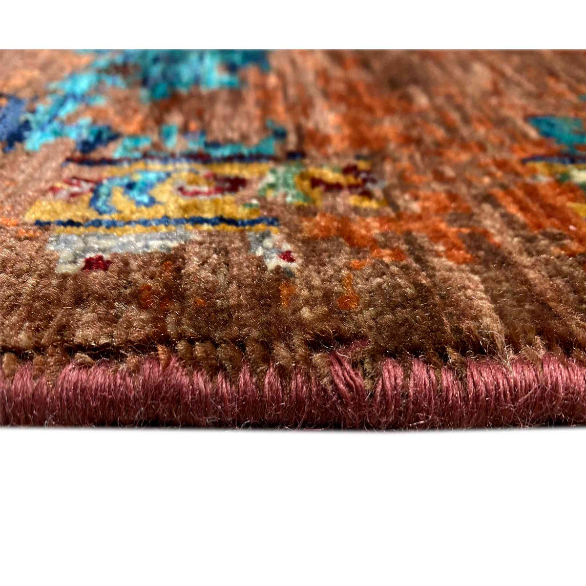 Rug edge with pile and a colorful pattern in rust brown and turquoise blue, with short fringes