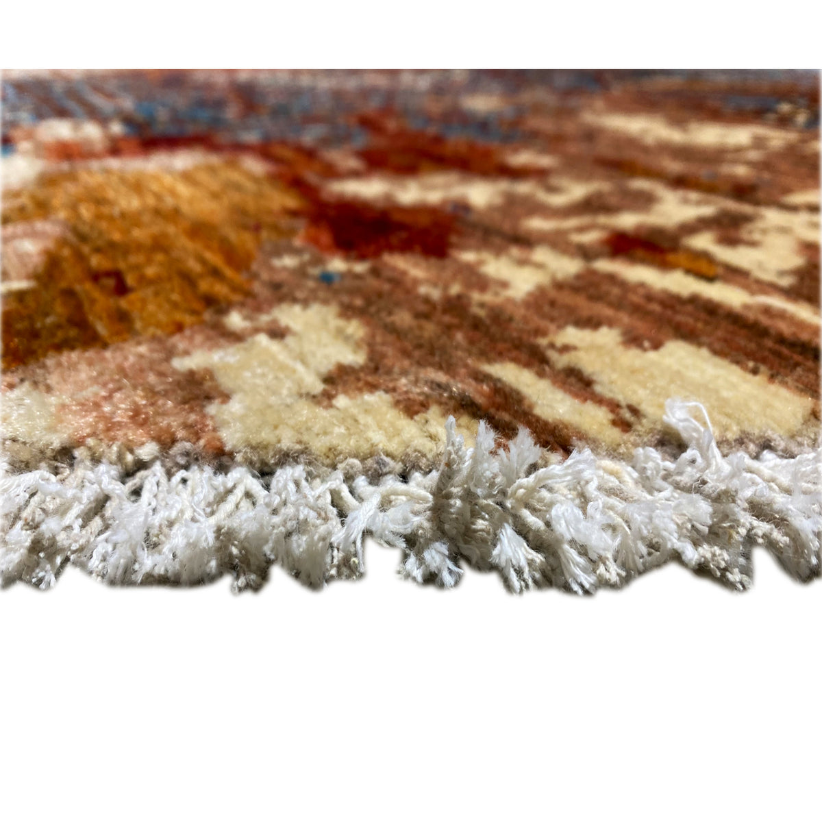 Rug edge with tassels: white-grey pile along a beige and brown patterned border