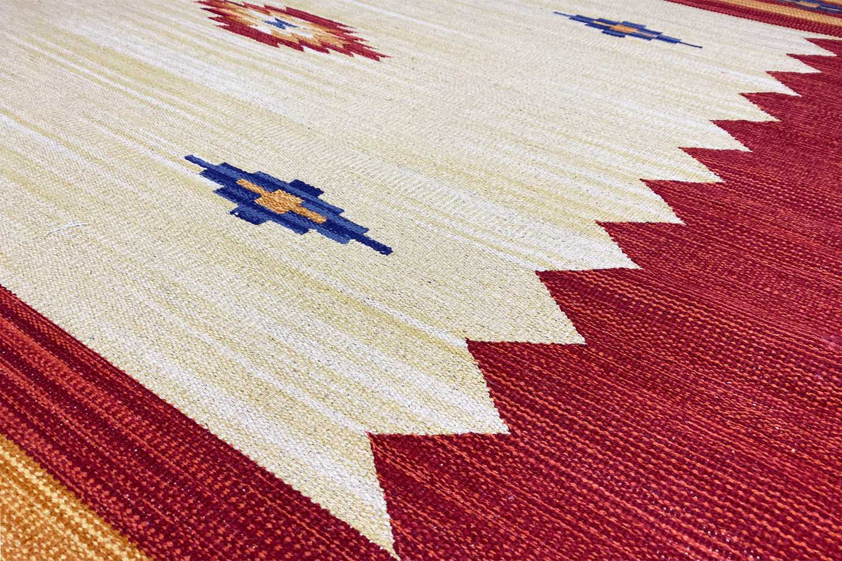 Kilim rug detail: beige pile with a red border, geometric blue shapes, and texture