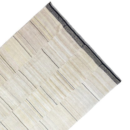 Corner of the kilim rug with a cream-colored pattern and dark gray border trim