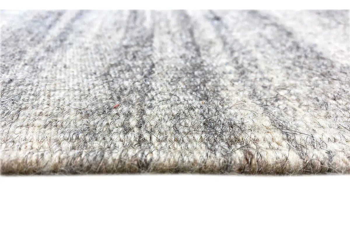 Close-up of the rug’s edge: fringes and a marled beige-gray texture