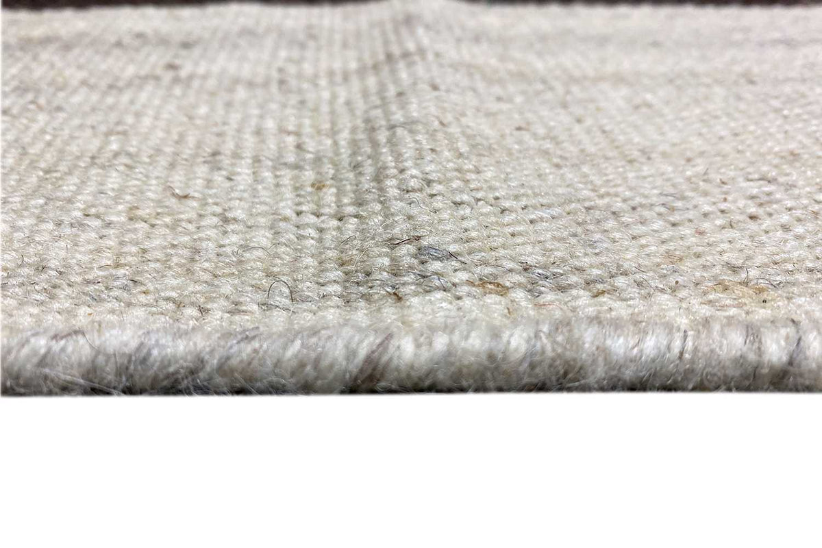 Close-up of a kilim rug: light beige pile with a bound, slightly frayed edge.