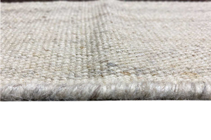 Close-up of a kilim rug: light beige pile with a bound, slightly frayed edge.