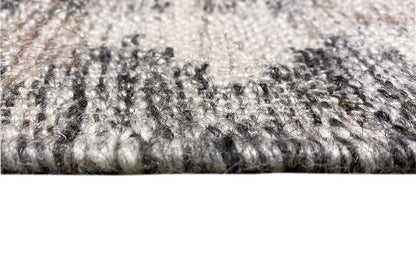 Close-up: rug edge with a fine pile and fringe, light gray with darker accents